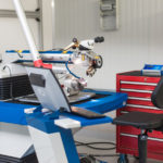 Ein modernes ALPHA Laser Schweißgerät in einer Werkstattumgebung. Das Gerät ist mit einem Mikroskop ausgestattet und für präzise Schweißarbeiten optimiert. Im Vordergrund steht ein Laptop für die Steuerung, daneben ein ergonomischer Arbeitsstuhl und eine rote Werkzeugschublade für Zubehör.