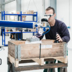 Mobiles Laserschweißgerät wird am Werkstück ausgerichtet, Schweißer trägt eine Schutzbrille und schaut durch das Okular.