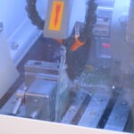 Metallprobe wird unter laufender Kühlmittelzufuhr mit einer Trennscheibe geschnitten, aufgenommen durch das Sichtfenster der geschlossenen Schutzhaube.