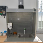 Arbeitsbereich mit Laborabzug, Spüle, Seifenspender und Belüftungsschacht – genutzt zur sicheren Reinigung oder chemischen Behandlung von Werkstoffproben.