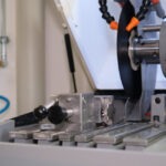 Nahaufnahme der eingespannten Werkstoffprobe in einer Trennmaschine, kurz vor dem Schneidvorgang mit rotierender Trennscheibe.