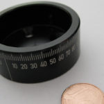 Eingravierte Meßskala am Umfang eines runden Bauteils, ein Cent-Stück liegt zum Größenvergleich neben dem Bauteil.