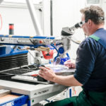 Mitarbeiter sitzt an einem Laserschweißgerät und schweißt Bauteil